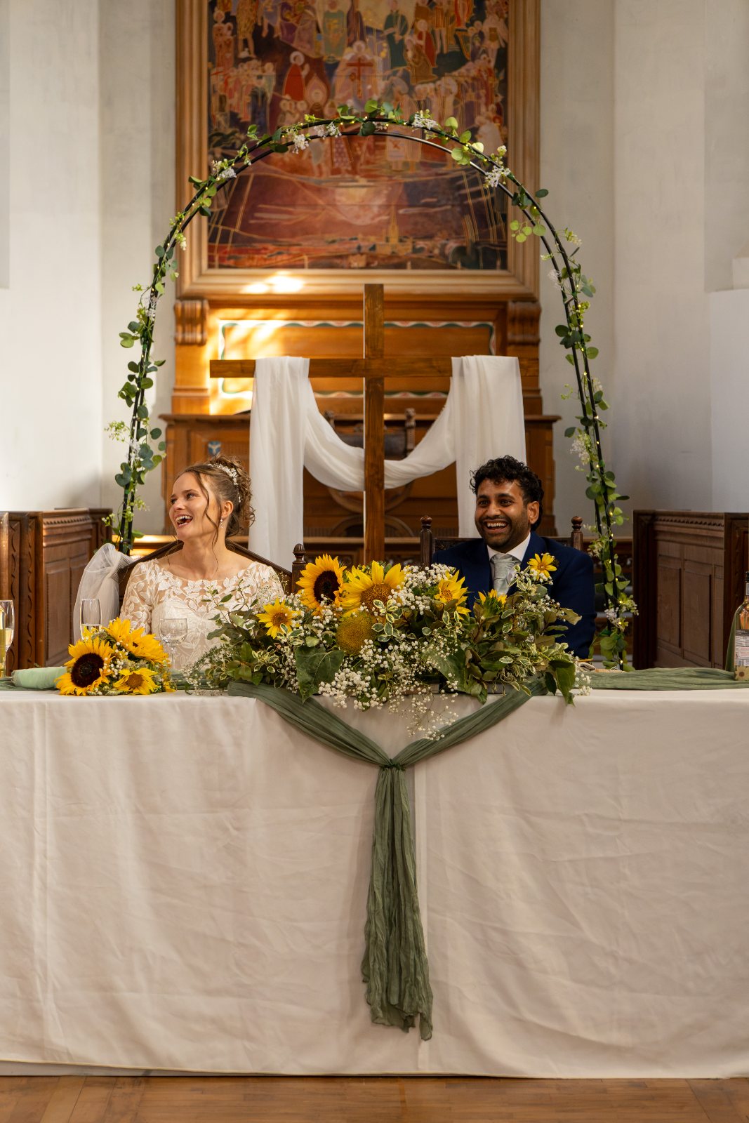 Katherine and Gurpreet laughing at the top table behind sunflowers